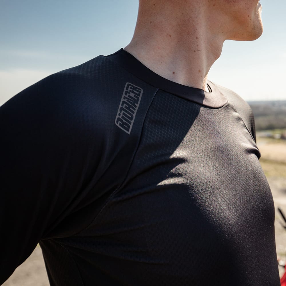 Close-up of a male cyclist wearing a black Bioracer Off-Road technical T-shirt, showcasing the shoulder logo and breathable fabric in outdoor sunlight.